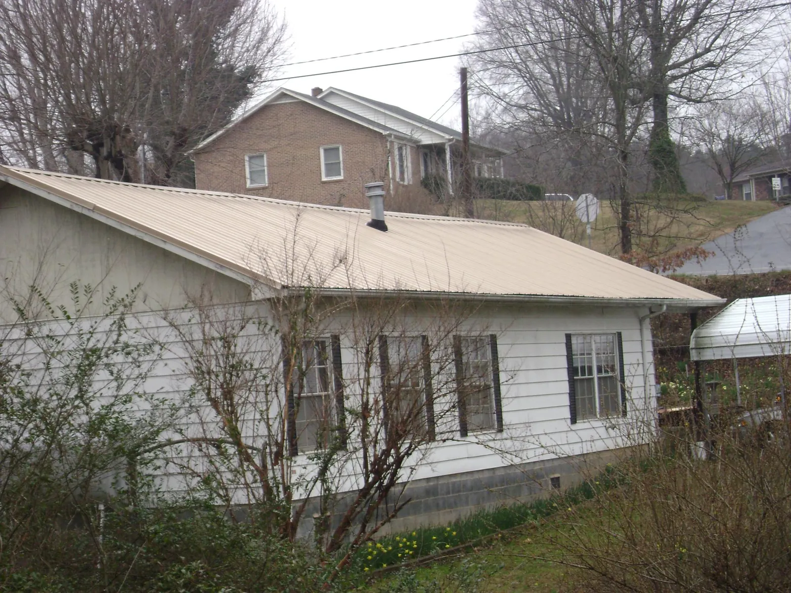 Tan metal roof on a white sided house set into a hillside — Commercial Roofing by Roofing Brothers in Westport